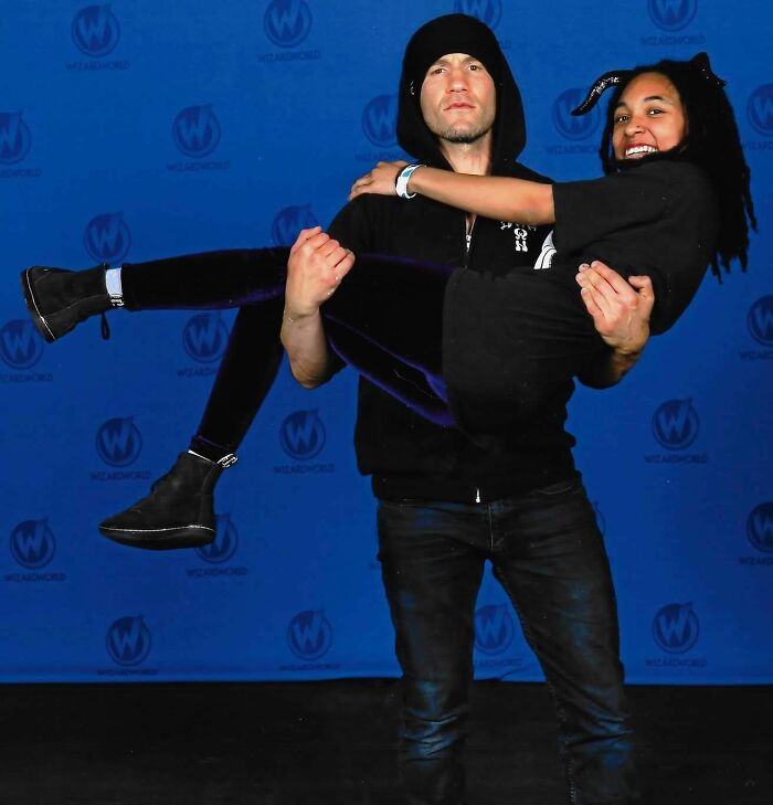 A person in a black hoodie smiling and holding up another person, showcasing a nice moment at a celebrity event.