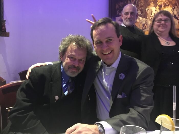 Two people smiling at a dinner table, with two others posing playfully in the background.