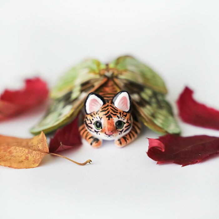 Pocket-sized animal figurine of a tiger with moth wings, surrounded by autumn leaves.