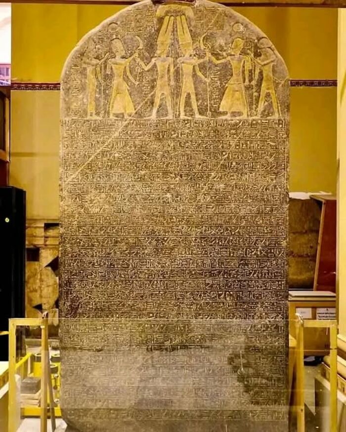 Ancient stone tablet with hieroglyphic inscriptions and carved figures displayed in a museum setting.