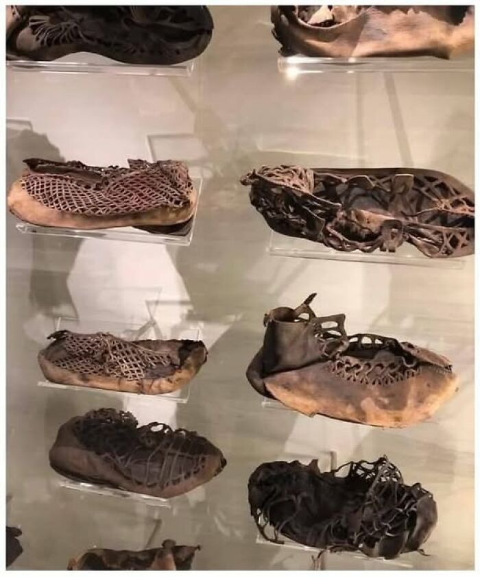 Ancient archaeological leather shoes with intricate lacing patterns displayed in a museum case highlighting historical architecture.
