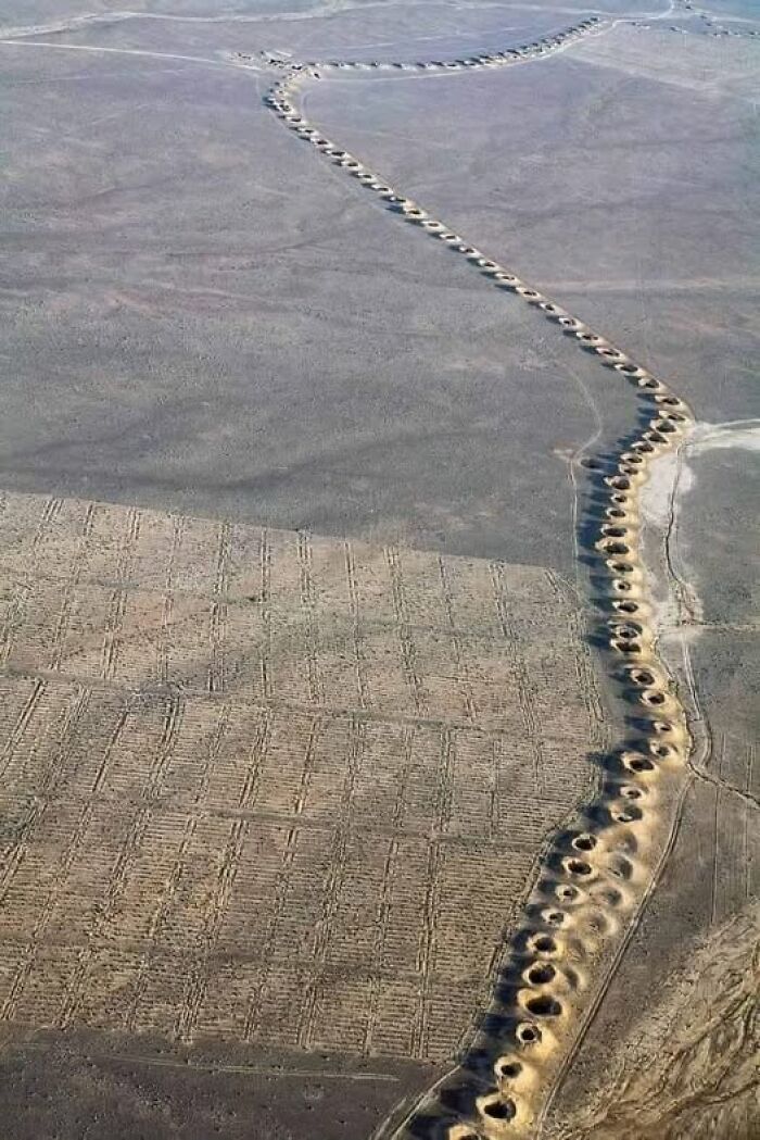 Aerial view of ancient archaeological trenches and earthworks forming a winding pattern in a barren landscape.