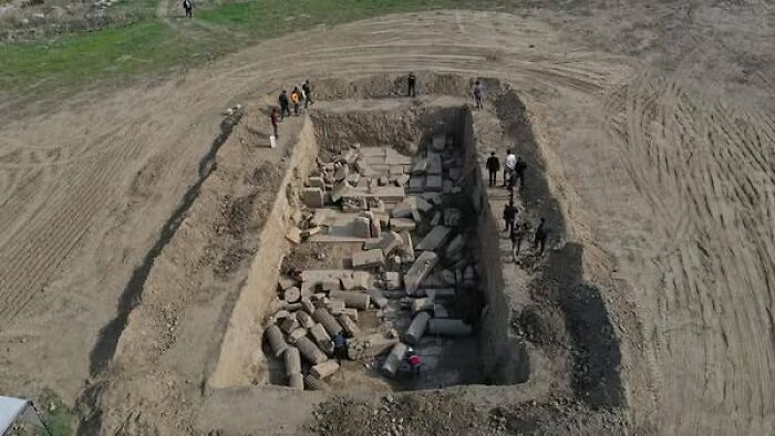 Aerial view of an archaeological excavation site with ancient stone ruins and several people exploring the area.