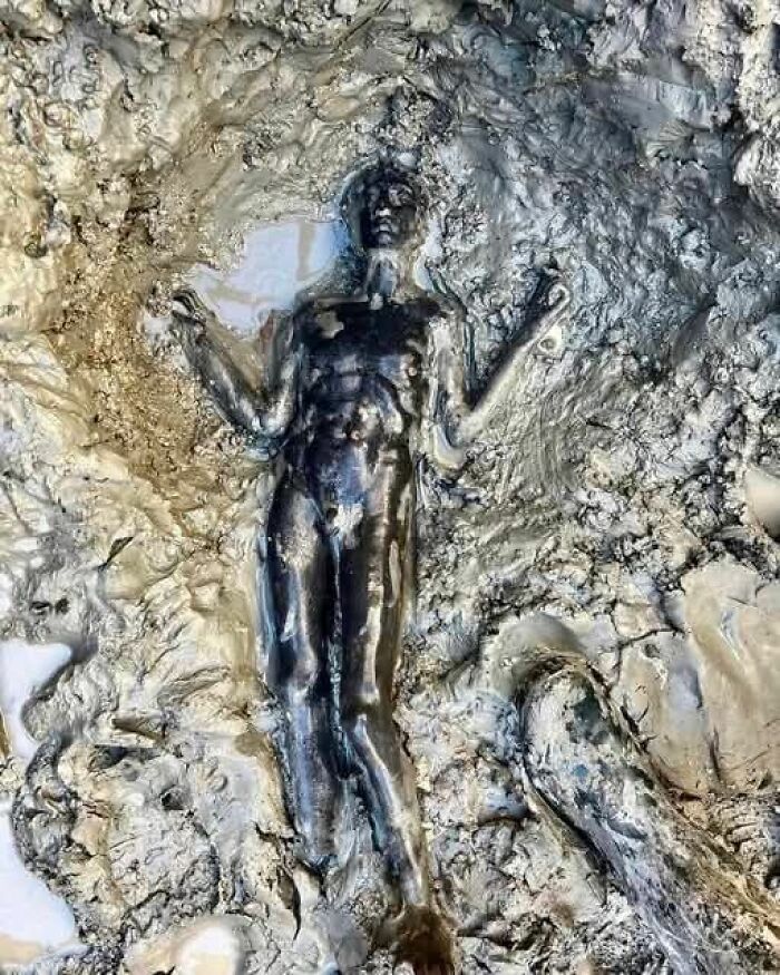 Ancient bronze statue partially uncovered in mud, showcasing detailed craftsmanship in archaeology news and architecture discovery.