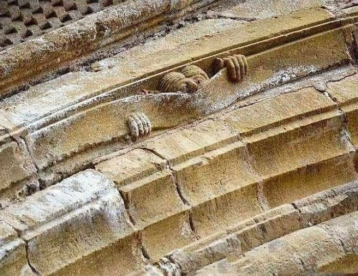 Stone carving of a figure peeking from an architectural arch, showcasing detailed craftsmanship in archaeology and architecture.