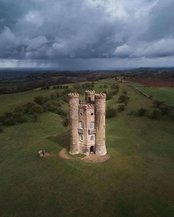 Medieval castle tower ruins on a grassy hill under stormy skies, showcasing archaeology and historic architecture details.