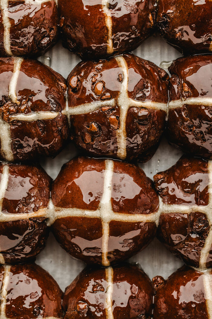 Shiny chocolate hot cross buns arranged in a neat pattern, showcasing food photography artistry.