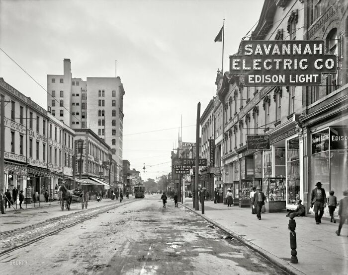 Historic black and white photo showing life in America with streetcars and pedestrians on a city street.