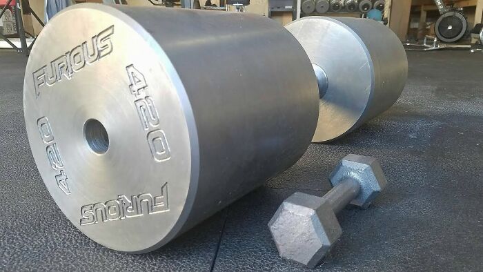 Oversized dumbbell next to a regular one on a gym floor, showcasing real unusual fitness equipment.