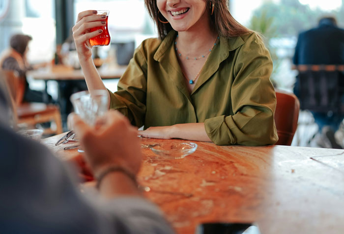Woman in green shirt smiling over drinks at a table, depicting love and proposal theme.