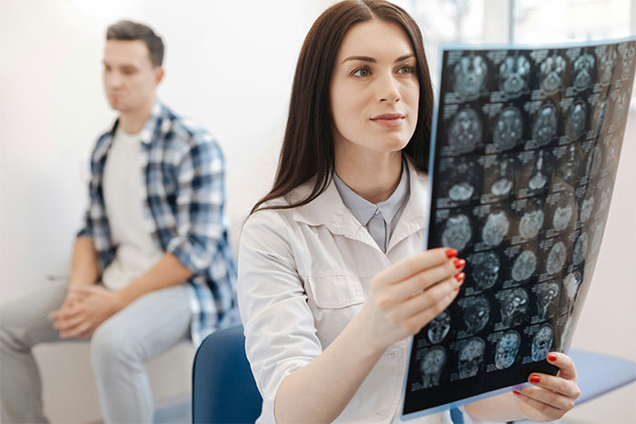Doctor examines brain scan while a concerned man sits in the background, related to anger incident.