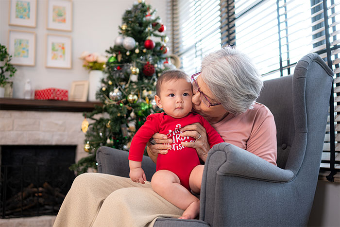 Grandmother kisses grandson on the cheek by a Christmas tree in a cozy living room.