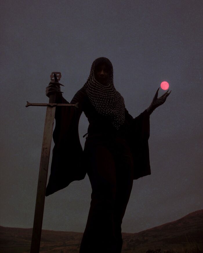 A figure in medieval armor holds a sword and a glowing orb, exemplifying dreamy dark escapism photography.
