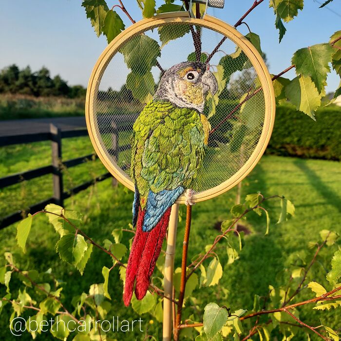 Embroidery of a colorful parrot in a hoop among leaves, showcasing intricate needlework art.