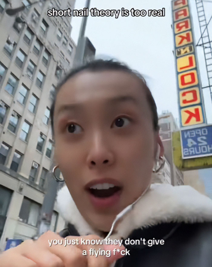 Young woman discusses short-nail theory, sparking patriarchy debate, as she walks city street with buildings in background. Young woman discusses short-nail theory, sparking patriarchy debate, as she walks city street with buildings in background.