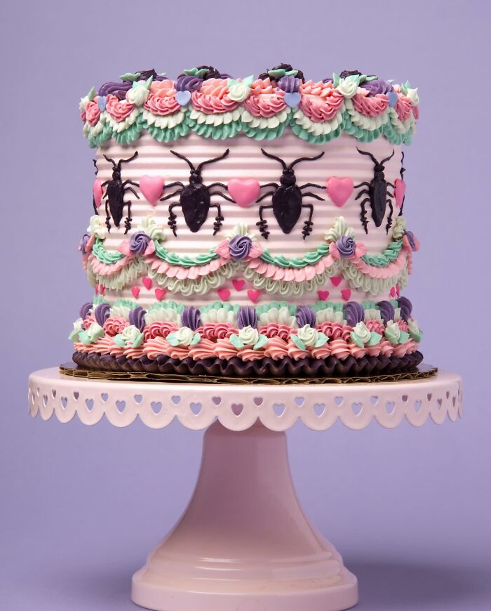 Vegan cake adorned with colorful frosting and black bug decorations on a white stand.