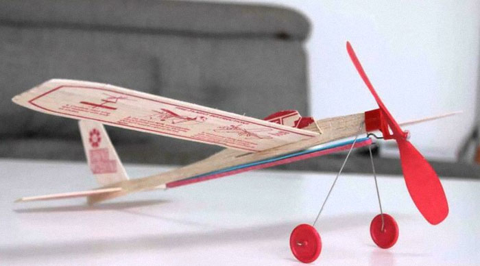 Toy plane with red propeller and wheels on a white table, evoking nostalgia.