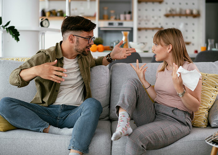 Man and woman having a heated discussion on a gray couch at home.
