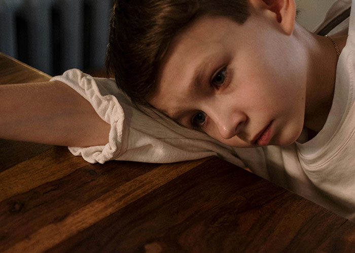 Sad child resting head on table, illustrating impact of negative teacher experiences.