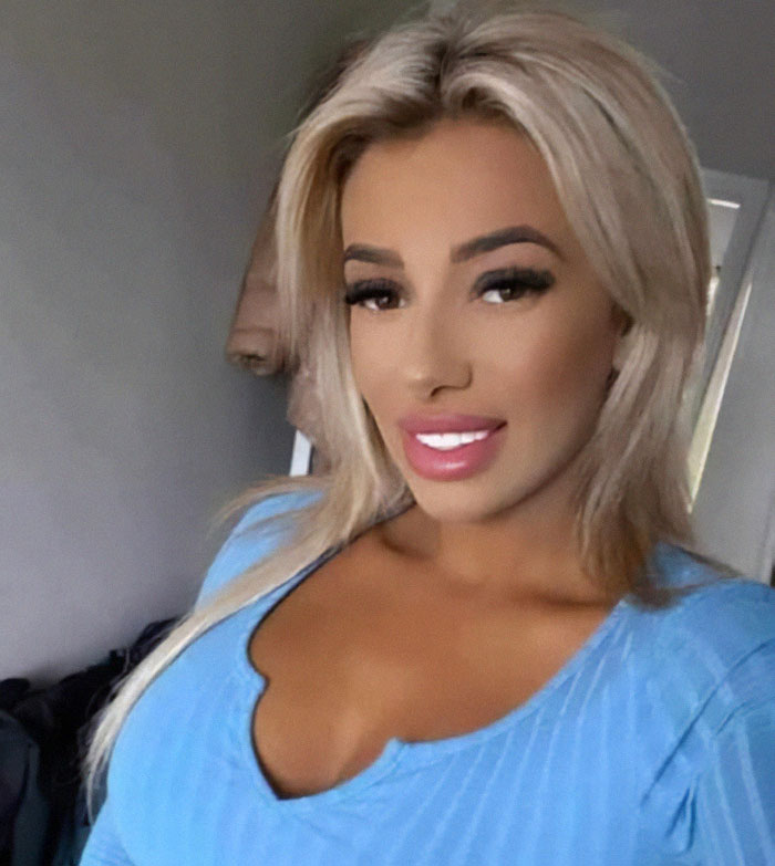 Young mom in a blue top, smiling, captures a selfie indoors before tragic event involving imposter surgeon.