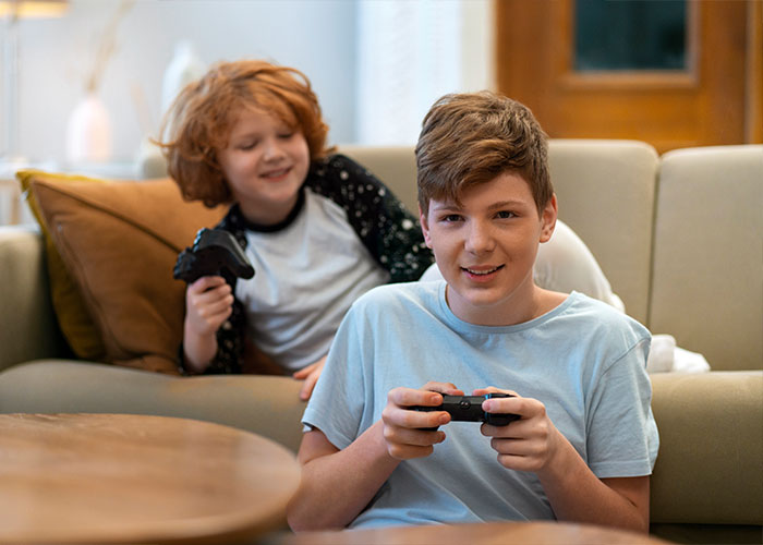 Two kids playing video games on a couch, smiling.