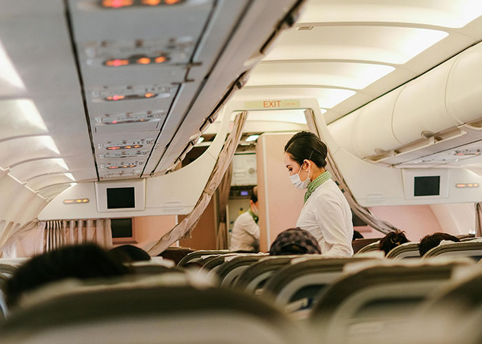 Flight attendant wearing a mask, attending to passengers in the cabin of an airplane.