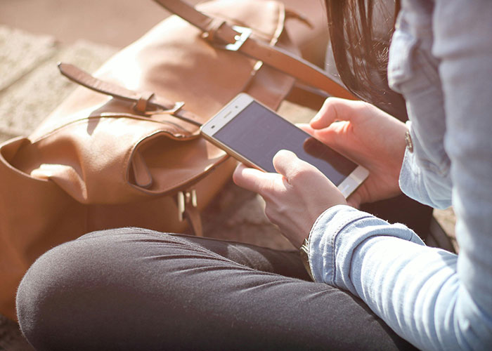 Person holding smartphone with brown leather bag nearby, reflecting on heartbroken people revealing cheating signs.