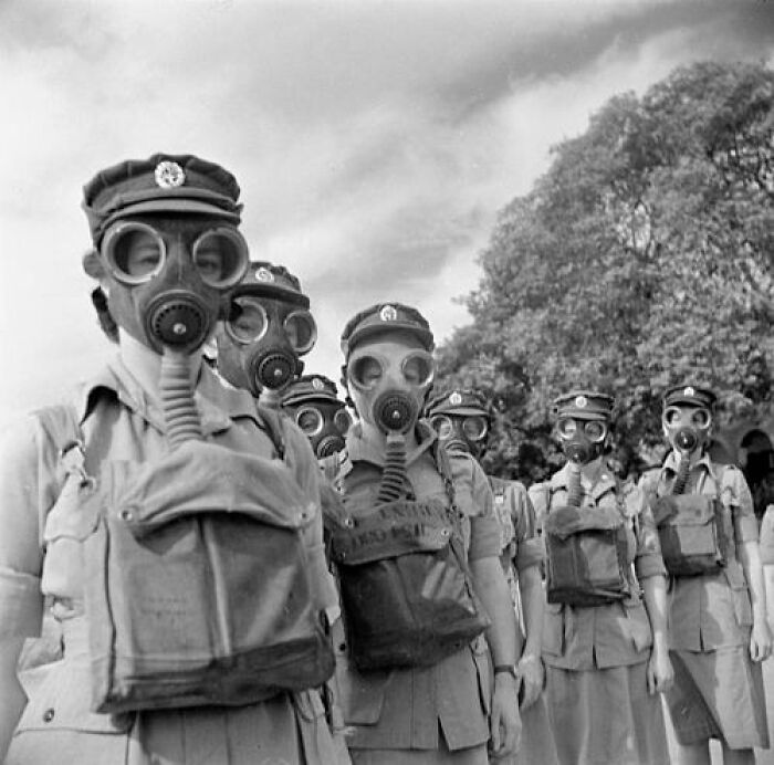 Soldiers wearing gas masks during WWII, standing in formation outdoors.