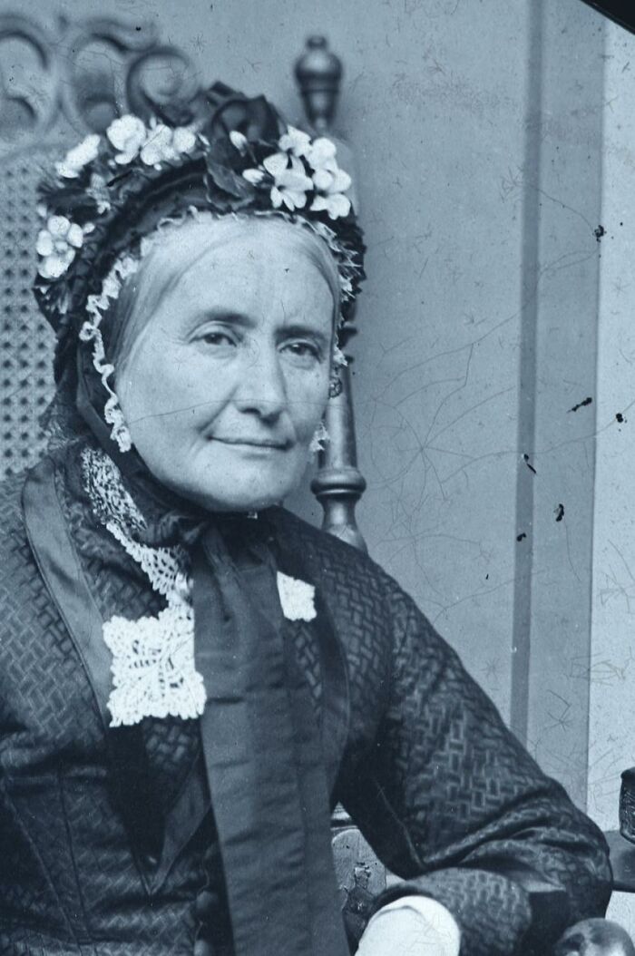 Elderly woman in vintage attire with floral bonnet captured in rare photographs restored from glass negatives.