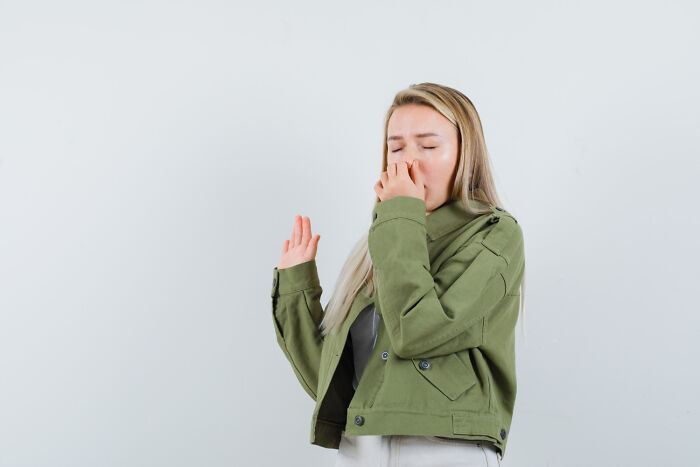 Person in a green jacket holding nose, reacting to strong odor, highlighting cleaning rules importance.