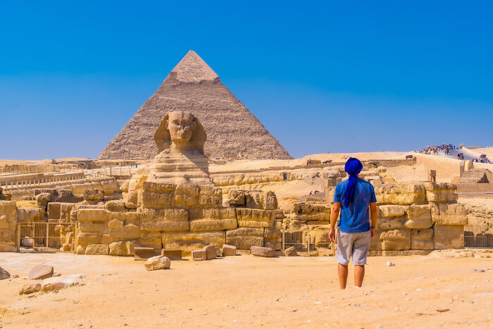 Person in blue shirt and hat, standing before the Sphinx and Pyramid, evoking a sense of instinctive awe and exploration.