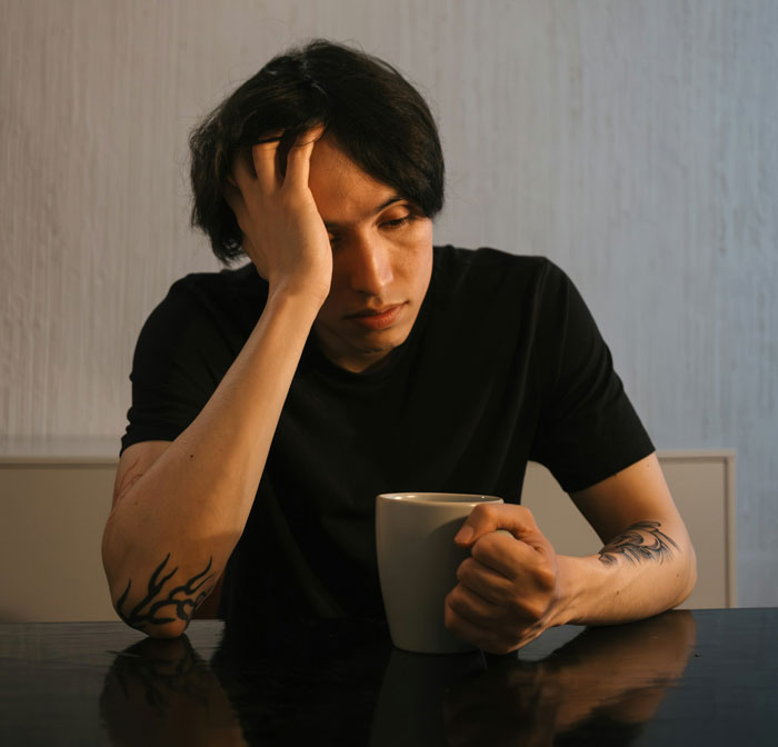 Man holding a mug, looking thoughtful after girlfriend defends against brother's prank.