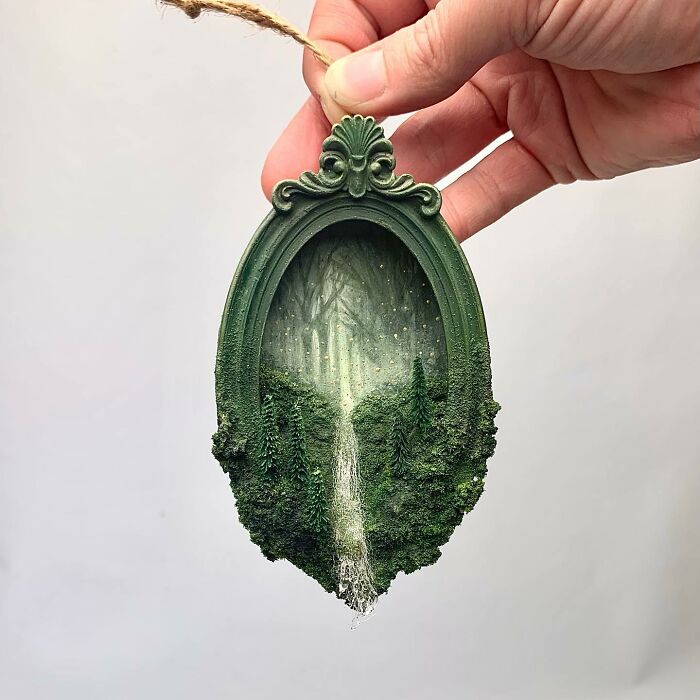 Hand holding a miniature diorama depicting a mystical forest scene with waterfall, ideal for alien and mystery aficionados.