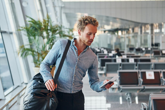 Man in airport reading travel documents, carrying a bag, illustrating American travel behavior.