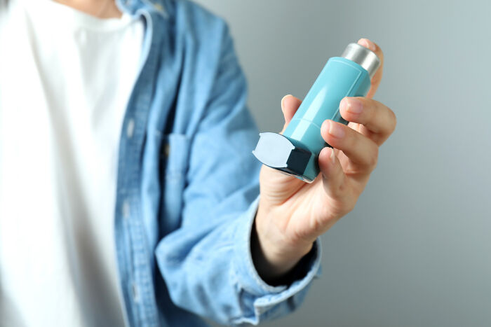 Person in a denim shirt holding a blue asthma inhaler, related to memorable high school incidents.