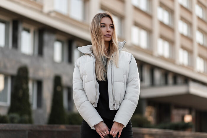 Young woman in a stylish white puffer jacket stands outside, exemplifying affordable treats in fashion.