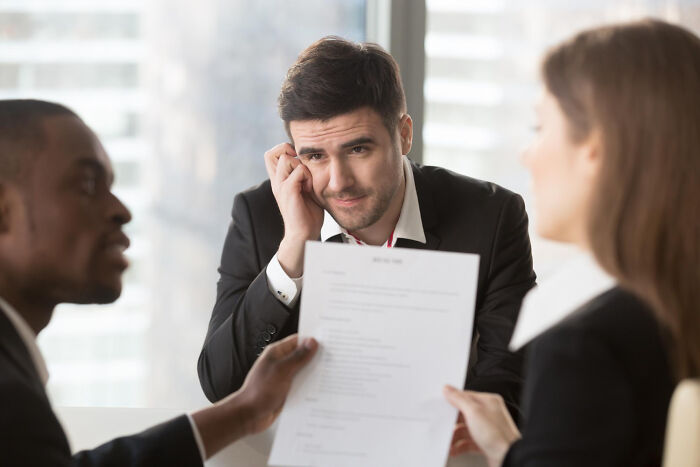 Man in a job interview looking confused while interviewers hold a paper, illustrating ridiculous interview questions