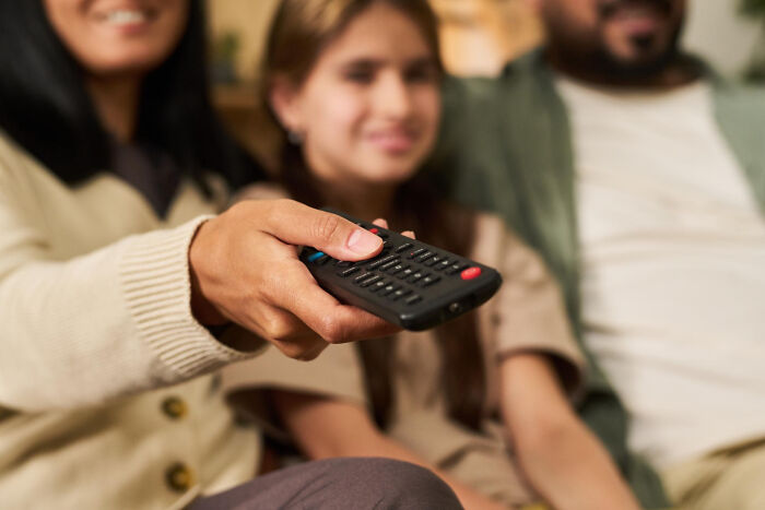 Family on a couch, remote in hand, highlighting bizarre house rules around TV time.