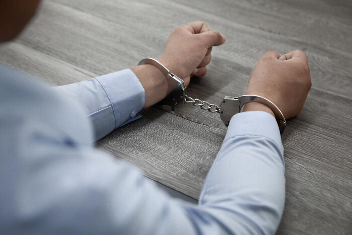 Person in handcuffs wearing a light blue shirt, sitting at a wooden table, evoking themes of regret and consequences.