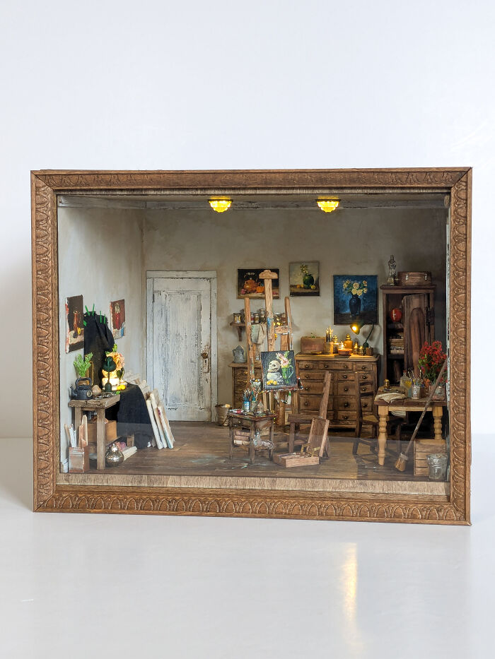 Miniature art studio in a wooden frame, featuring tiny furniture and paintings, capturing a detailed tiny world.