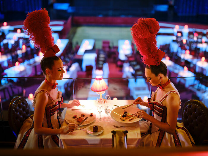 Two women in elaborate costumes dining elegantly with wine, showcasing culinary art for the World Food Photography Awards.