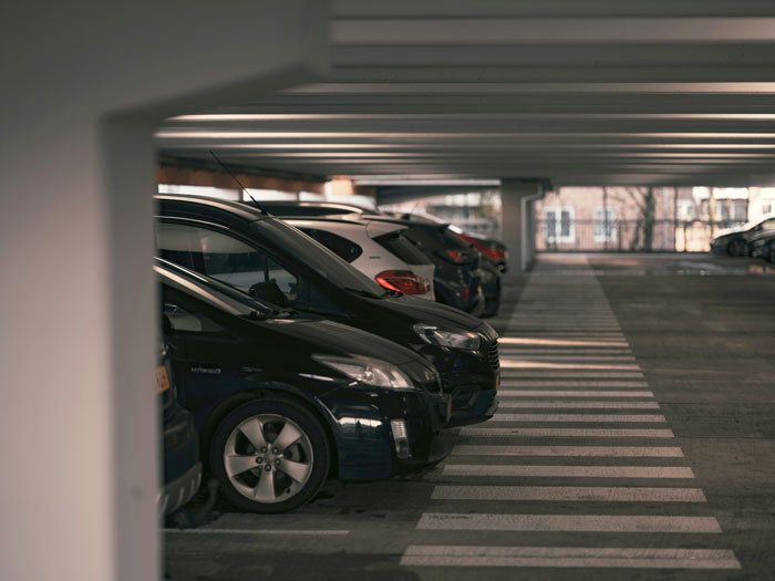 Cars parked in a dimly lit parking garage with rows of vehicles along marked parking spaces and lanes.