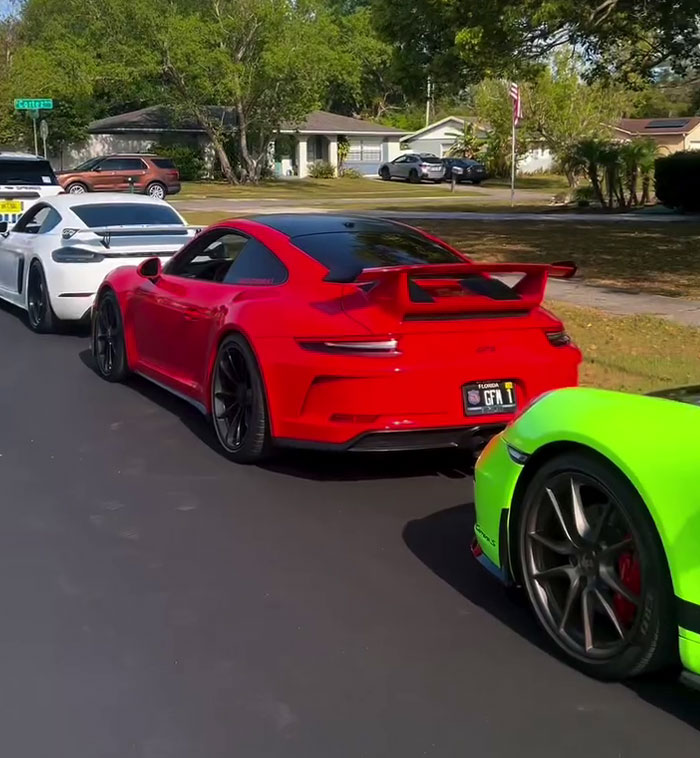 Sports cars lined up on a residential street, featuring a red car in the center.
