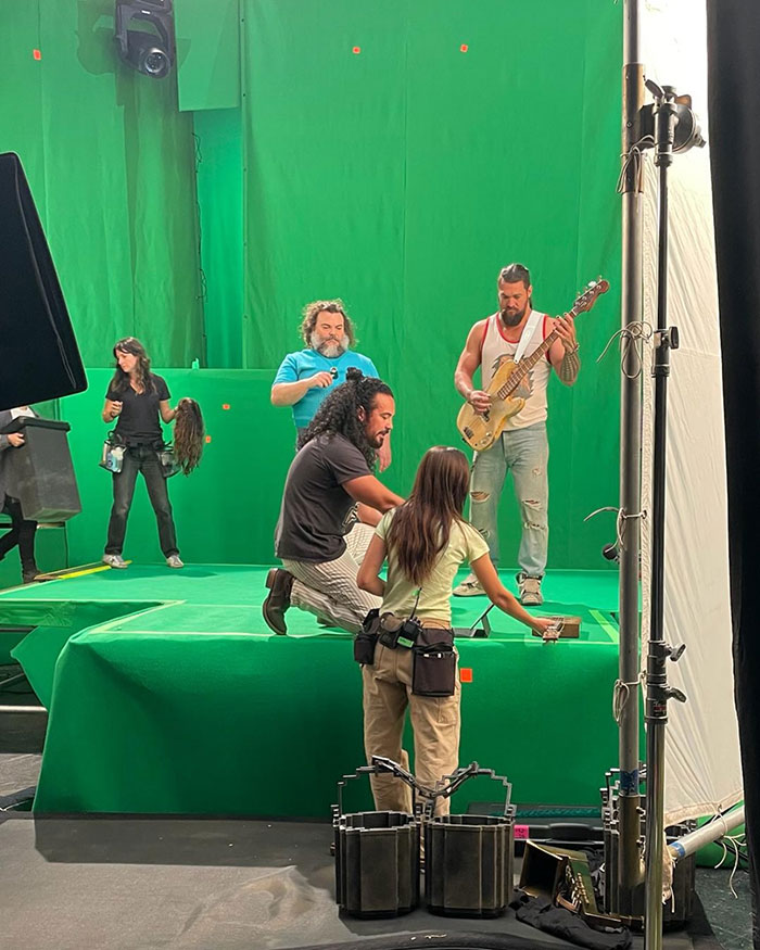 People on a green screen set, one holding a guitar.
