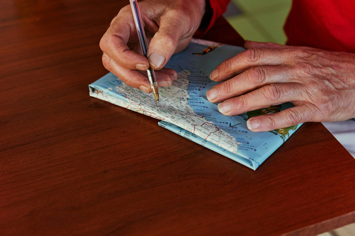 Hands holding a pen over a map, highlighting travel routes, emphasizing closeness to parents through travel planning.
