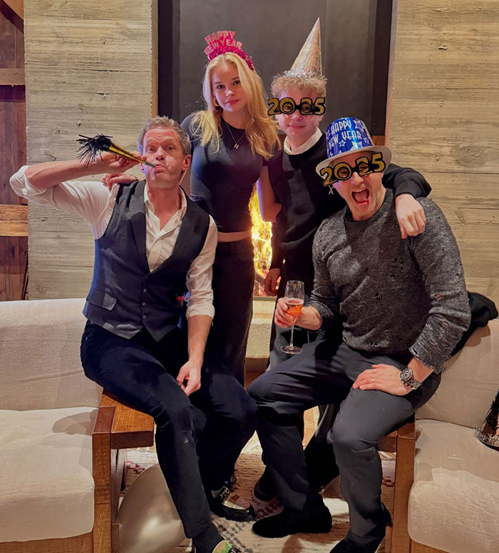 People celebrating New Year's Eve in festive hats, gathered around a fireplace, enjoying the evening together.
