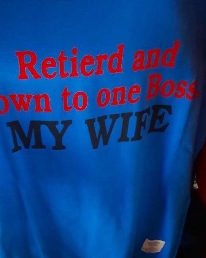 Blue T-shirt with humorous translation error saying "Retierd and down to one Boss, MY WIFE" seen in bright lighting.