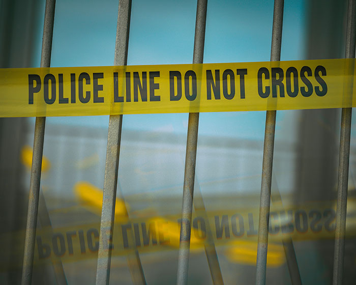 Yellow police tape with "Do Not Cross" text on metallic fence rails.
