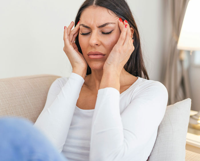 Woman in white shirt on a sofa, looking shocked after receiving family DNA results.