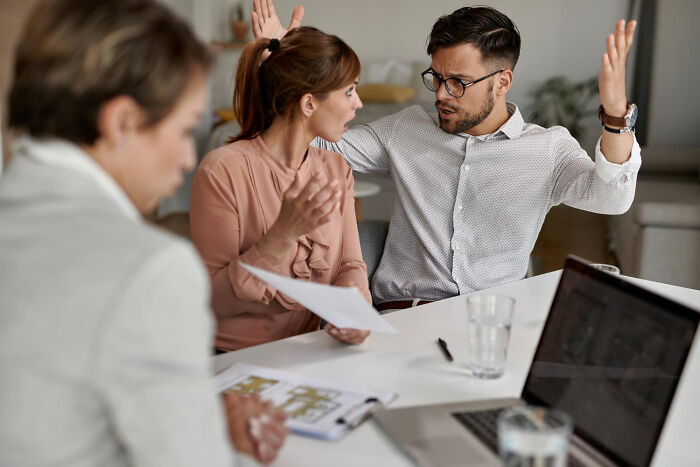 Office conflict with three colleagues at a table during an intense work drama discussion.